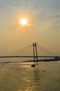 Silhouette bridge over sea against sky during sunset