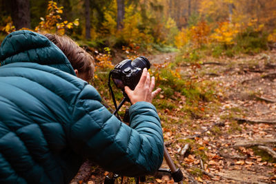 Full length of man holding camera in forest