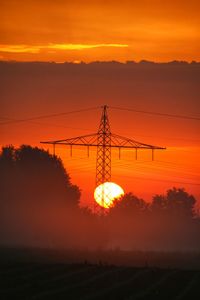 Silhouette electricity pylon on field against romantic sky at sunset