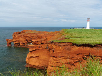 Lighthouse on rock by sea against sky