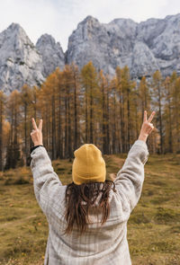 Rear view of young woman with raised arms standing under beautiful mountains in autumn