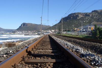 Railroad tracks by mountain against clear sky