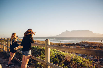 Women leaning on railing against clear sky