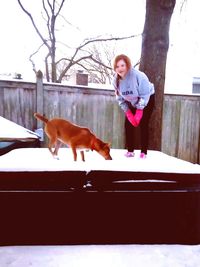 Portrait of young woman with dog standing against bare trees