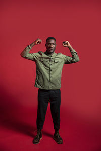 Full length portrait of man standing against red background