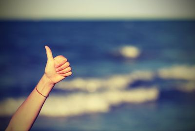 Cropped hand of woman gesturing by sea against sky