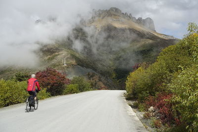 Rear view of man riding bicycle on road leading towards mountain during foggy weather