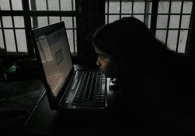 Side view of girl using laptop at home