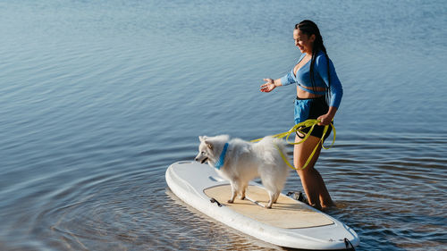 Woman preparing to paddleboarding with her dog japanese spitz sitting on sup board on the lake	

