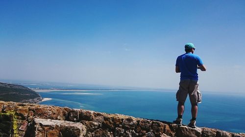 Rear view of man standing on rock against sea