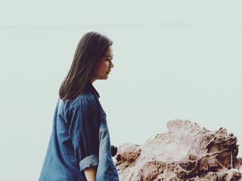 Side view of thoughtful young woman standing by rock