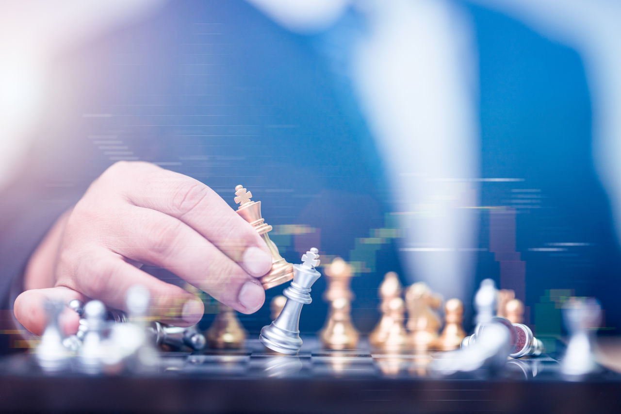 CLOSE-UP OF MAN PLAYING WITH CHESS PIECES ON BACKGROUND