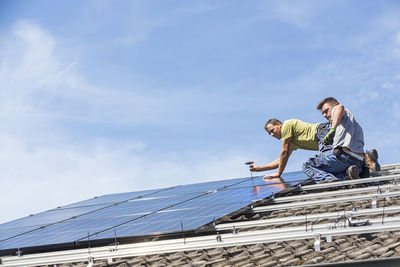 Low angle view of men working on roof against sky