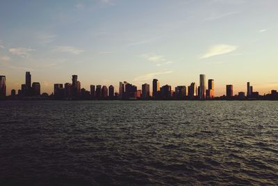 City buildings by sea against sky during sunset