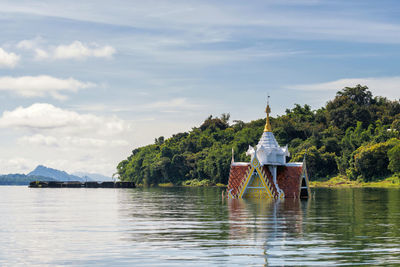 Gazebo by lake and building against sky