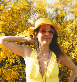 Young woman wearing hat standing against yellow flowers