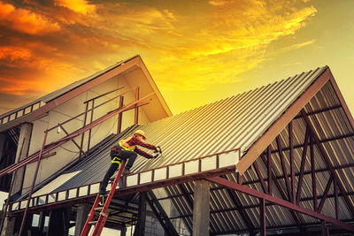 Low angle view of men working on building against sky