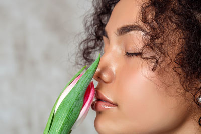 Close-up of beautiful woman smelling tulip against wall