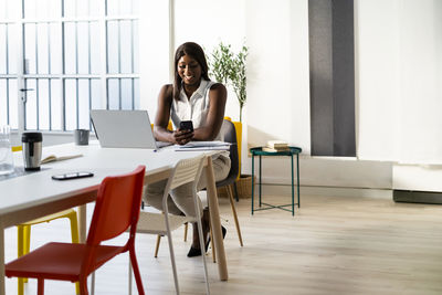 Young woman using phone while sitting on table