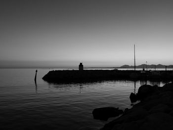 Silhouette people on rock by sea against clear sky