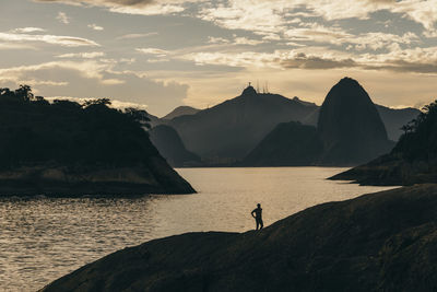 Silhouette man standing on rock by sea against sky during sunset