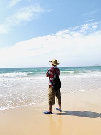 Rear view of young man with backpack standing at beach against sky