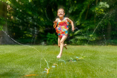 Child jumping and playing through a sprinkler in a backyard on a sunny day