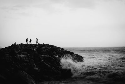 People standing on rock by sea against sky