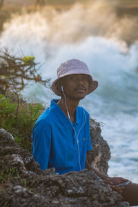 Side view of young man standing by ocean using a mobile phone