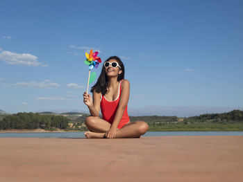 Portrait of young woman sitting on beach against sky