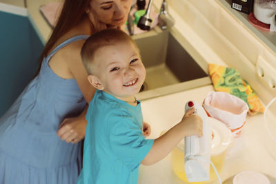 High angle portrait of smiling son preparing food while standing with mother in kitchen