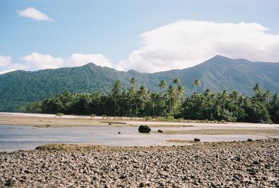 Scenic view of tropical beach with palm trees against sky. mountins on background