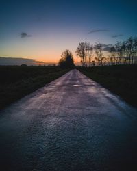 Road amidst silhouette trees against sky during sunset