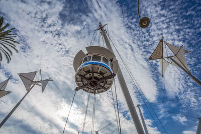 Low angle view of electric lamp hanging by building against sky