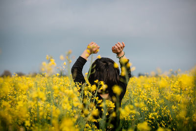 Rear view of small child  standing with raised arms in the field with yellow flowers