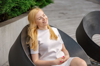Young beautiful blond woman sitting outdoors, on the wooden terrace in the city and resting