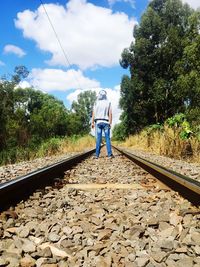 Rear view of man standing on railroad track against sky