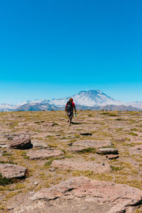 Rear view of male hiker walking on mountain against clear blue sky