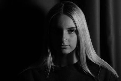 Close-up portrait of young woman wearing nose ring in dark