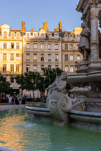 Statue by fountain in city against sky