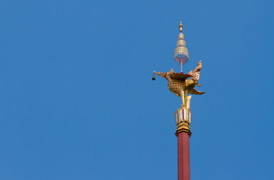 Low angle view of statue by building against clear blue sky