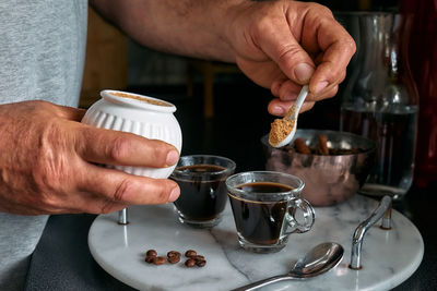 Man preparing classic italian coffee in the mocha and pouring sugar into coffee in small coffee cup.