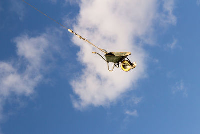 Low angle view of wheelbarrow against blue sky and clouds