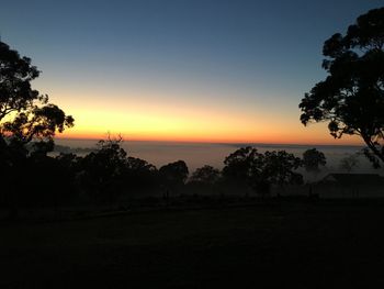 Silhouette trees on landscape against sky during sunset
