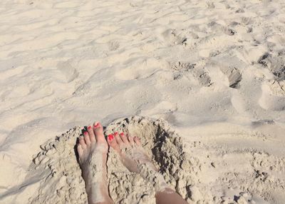 Bare feet and red nailpolish on sand at beach