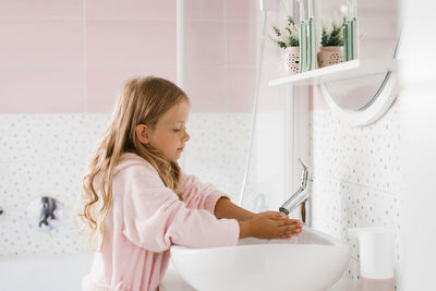 Little girl in a pink bathrobe washes her hands in the bathroom