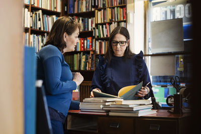 Female customer discussing with librarian standing in bookstore