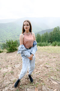 A young girl with long hair in jeans stands in a beautiful nature. behind her mountains