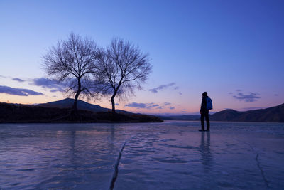 Silhouette mature man standing on frozen lake against sky during sunset