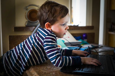 Side view of boy using laptop at home
